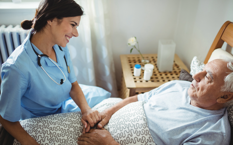 Free from manual vital sign documentation, a nurse spends time with an elderly male patient at his bedside.