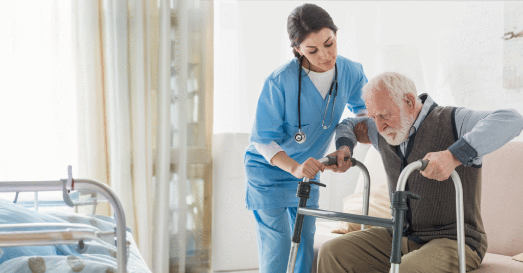 A clinician in a skilled nursing facility helps an elderly male patient transitioning to the facility stand using a walker.