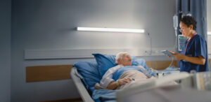 Nurse reviewing patient data on a tablet during bedside rounds with an elderly resident in a skilled nursing facility