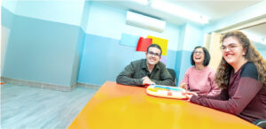 Residents of an IDD group home sit at a table playing an electronic game.