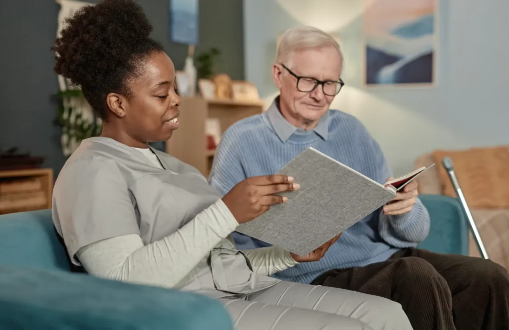 Health aide in a memory care center looks at a photo album with a male resident.