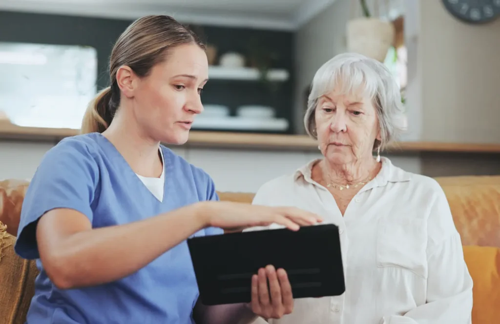 Female hospice nurse explains what the data is showing as she meets with an elderly woman in her home.