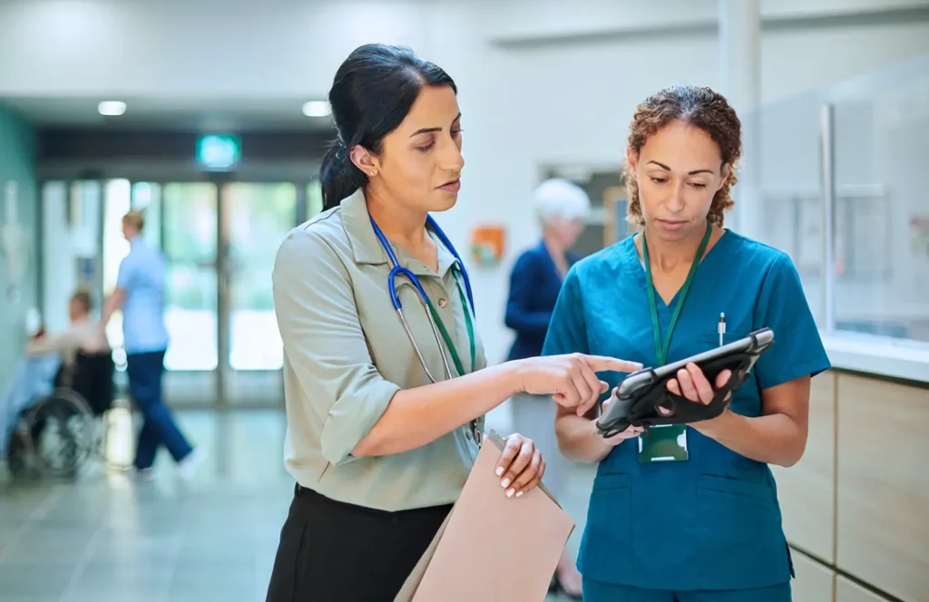 Physician and medical assistant reviewing patient trends on a tablet.